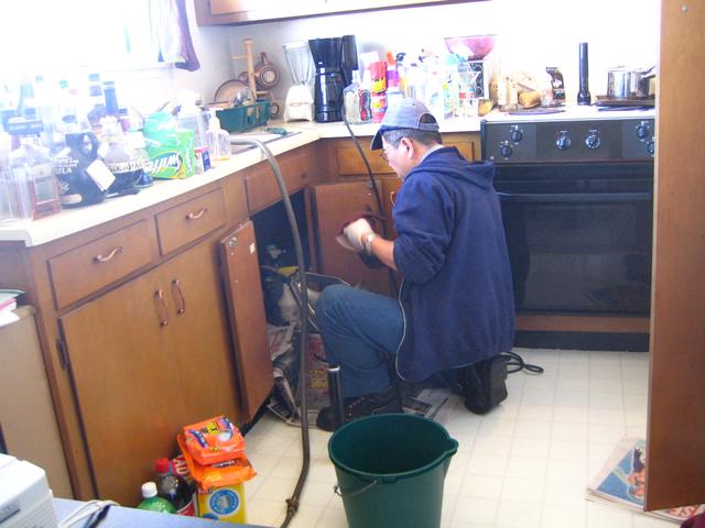 Plumber working under a kitchen bench with tools on the floor