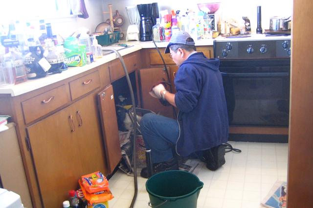 Plumber working under a kitchen bench with tools on the floor