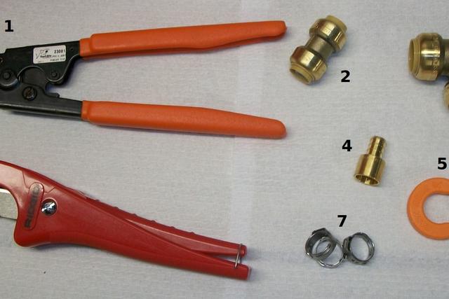 Pipe cutter, crimping tool and brass fittings laid out for a water pipe repair